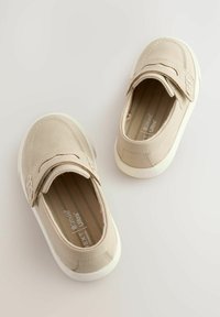 Beiga kanvas slip-on skor med rund tå, vit gummisula och dekorativ sömnad. Justerbar rem för säker passform.