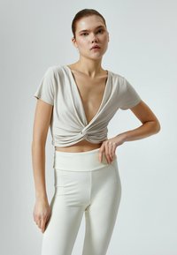 Lys beige cropped top med dyb V-hals og snoet frontdesign, parret med højtaljede hvide leggings, glat tekstur, tætsiddende silhuet.