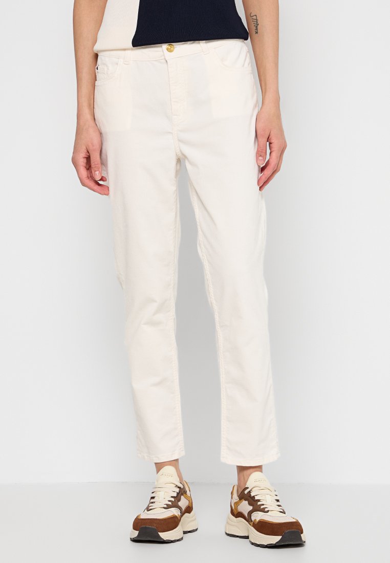 Kremowe, zwężane spodnie wykonane z lekkiego materiału, z kieszeniami z przodu i metalowym guzikiem. Noszone z brązowo-beżowymi sneakersami.
