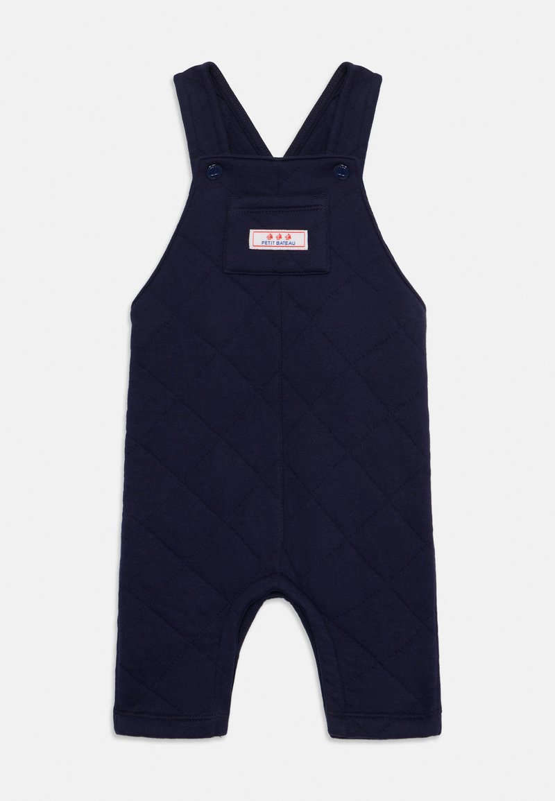 Tengerészkék steppelt overall, állítható pántokkal, elülső zsebbel, melyen címke található, és hemzélt szélekkel. Kivágott lábak a mozgás szabadságáért.