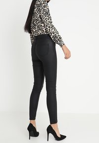 Černé skinny kalhoty s hladkým povrchem, s vysokým pasem a klasickým pětikapsovým designem. Doplněné o dlouhý leopardí top.