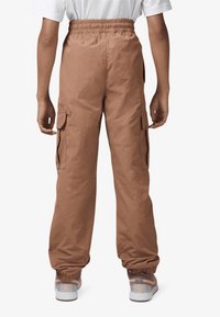 Lichte bruine cargobroek van een lichtgewicht stof, met een elastische tailleband, zijzakken en elastische boorden. Gekenmerkt met witte sneakers.