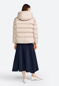 Lichtbeige pufferjack met capuchon, voorzien van een doorstikt ontwerp en een cropped silhouet, gecombineerd met een donkerblauwe lange rok en witte flats.