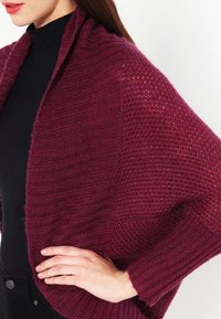 Burgunderroter Strickschal mit unterschiedlichen Texturen; verfügt über ein lockeres, drapiertes Design, Rippen- und Offenstrickmuster, die für geschichtete Wärme sorgen.