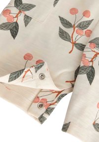 Indumento in cotone con base crema che presenta un motivo floreale di ciliegie rosa e foglie verdi; dotato di bottoni a pressione all'orlo.