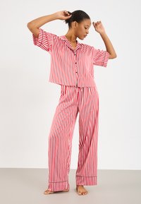 Red and white striped pajama set, short-sleeved button-up top, loose-fitting pants with black accents and a drawstring waist. Smooth texture.