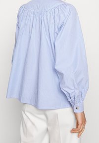 Blusa in cotone a righe blu e bianche con schiena arricciata, maniche a sbuffo e polsini abbottonati. Vestibilità rilassata con orlo arrotondato.
