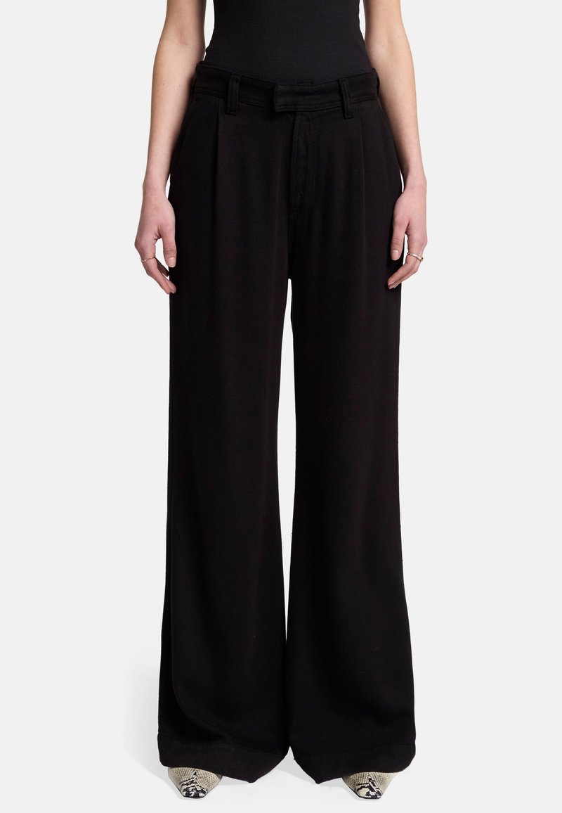 Pantalons larges noirs à taille haute, avec un devant plissé et un tissu lisse. Comprend des passants de ceinture et des poches latérales, se mariant bien avec des chaussures texturées.