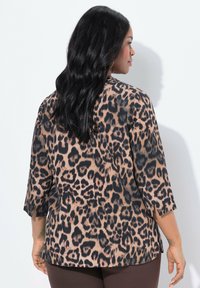 Blus med leopardtryck i beige och svart, med trekvartslånga ärmar och avslappnad passform, sidoflikar och smidig textur.