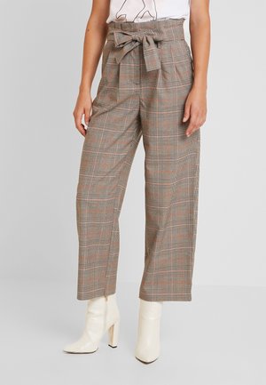 Pantalons marron à carreaux avec un lien à la taille, présentant une coupe ample et des jambes larges, associés à des bottines blanches.