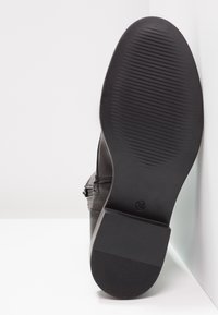 Semelle de chaussure en cuir noir avec texture striée. Caractérisée par un talon plat et un marquage de taille visible. Design simple avec bords lisses et sans embellissements.