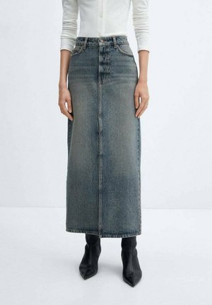 Femme portant une jupe maxi en jean bleu délavé taille haute avec une couture devant et des bottines noires à bout pointu.