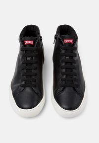 Zapatillas altas de cuero negro con suela de goma blanca, que presentan cordones negros, una cremallera en el lateral y un logo rojo de "Camper" en la lengüeta.