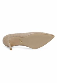 Scarpa nude con tacco a spillo e punta affusolata, con una texture effetto coccodrillo. Suola liscia di un colore beige chiaro.