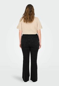 Top beige de manga corta con puños doblados, combinado con jeans negros de tiro alto y acampanados. Tejido suave, diseño ajustado con detalles de bolsillos.