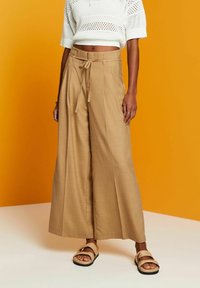Wide-leg pants in light brown fabric, featuring a high waist with a tie belt. Paired with a white, cropped knit top and beige sandals.