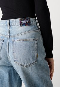 Hele sinine denimsärgid, mis on veidi lõdva lõikega, tagaküljel must label värvikate mustritega ja ainulaadsed lõikeaktsendid taskutel.