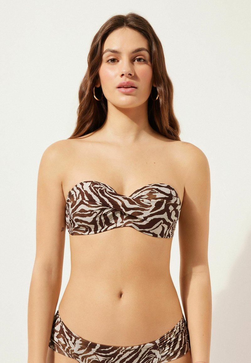Avtagbar bikiniöverdel i brun och beige zebramönster med tvinnad detalj fram. Slät, elastisk tyg. Accentuerad med medelstora hoops örhängen.
