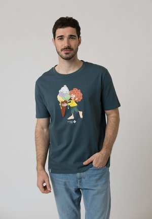 Mann trägt ein dunkelgrünes T-Shirt mit einer Cartoonfigur, die einen großen schmelzenden Eiskremkegel hält, kombiniert mit hellblauen Jeans.