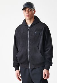 Crna zip-up dukserica izrađena od mekog suede materijala, s kengur džepom i rebrastim rubovima. Uključuje diskretan crni logo "Lakers".
