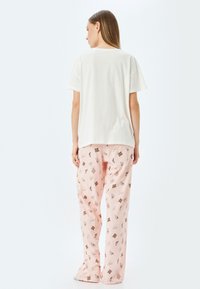 Vit oversized T-shirt med korta ärmar, kombinerad med ljusrosa pyjamasbyxor som har olika mönster av choklad och rosetter. Mjuk bomullstyg.