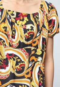 Robe à motifs floraux avec des manches courtes, présentant des tourbillons jaunes, orange, rouges et blancs sur un fond noir. Découpe carrée et tissu froncé.