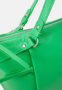 Sac à main en cuir vert avec bandoulière réglable, comportant une fermeture éclair et des garnitures argentées. Fini texturé avec des accents lisses.