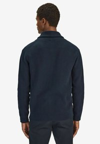 Marinblå ribbad stickad tröja med rundad krage och långa ärmar. Texturen är slät, med en figurnära design och synlig sömnad på axlarna.