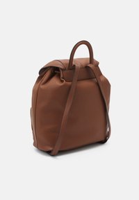 Sac à dos en cuir marron avec une forme structurée, doté d'un rabat supérieur et de deux poignées. Les accents comprennent des coutures discrètes et une poche zippée sur le côté.