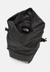 Černý batoh s rolovacím uzávěrem vyrobený z voděodolného materiálu; má přední zipovou kapsu a logo North Face na spodní části předního dílu.