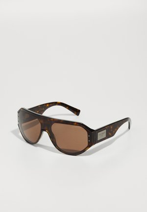 Óculos de sol em padrão tartaruga com lentes castanhas, formato octagonal, linha de sobrancelha proeminente e detalhe em metal com o logótipo na haste lateral.