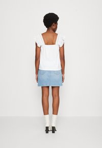 Hvid ærmeløs top med blondekant, kombineret med nederdel i lys blå denim i mini-stil og hvide ankelstøvler med blokk hæl.