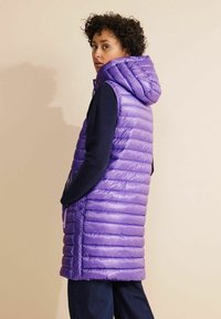 Lila puffig väst med huva, med vertikala kviltade sektioner, blixtlåsdetaljer på sidorna och en glänsande, slät yta.