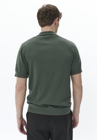 Camisa polo verde de manga corta con textura de punto, cuello estándar y puños acanalados. Diseño simple, sin patrones ni acentos visibles.