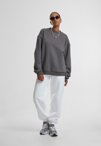 Grijze oversized sweatshirt met geribbelde manchetten, gecombineerd met witte joggers en grijze sneakers. Accessoires zijn onder andere een zwarte zonnebril en een zilveren ketting.