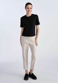 Czarny t-shirt z krótkim rękawem i jasnobeżowe, dopasowane spodnie, w zestawieniu z czarnymi zamszowymi butami. Gładka tekstura i dopasowany krój.