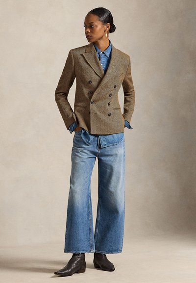 Καφέ σακάκι διπλής σειράς με σχέδιο ψαροκόκκαλο πάνω από τζιν πουκάμισο, συνδυασμένο με φαρδιές ξεβαμμένες μπλε τζιν παντελόνες και μαύρα μποτάκια αστραγάλου.