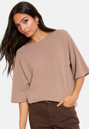 Helles, braunes Strickpullover mit weitem Ausschnitt und kurzen, lockeren Ärmeln, der ein strukturiertes Muster aufweist und mit braunen Hosen kombiniert ist.