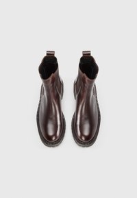 Bottines en cuir marron foncé avec des panneaux élastiques sur les côtés, des anses de traction et des semelles en caoutchouc épaisses et rainurées. Fini lisse avec des bouts arrondis.