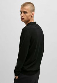 Schwarzer, langärmeliger Rundhalsausschnitt Strickpullover mit glatter Textur, der ein dezentes Logo auf dem Rücken und eine taillierte Passform aufweist.