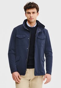 Granatowa lekka kurtka z zamkiem z przodu, dwoma kieszeniami na piersi i stojącym kołnierzem. Wykonana z gładkiego materiału o luźnym kroju.