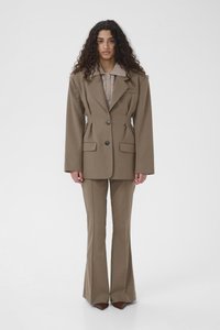 Καφέ σμόκιν σακάκι με μεγάλα πέτα και δύο κουμπιά, συνδυασμένο με αντίστοιχο παντελόνι καμπάνα. Υφασμάτινο μπεζ πουκάμισο από μέσα.