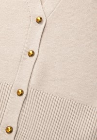 Cardigan beige con scollatura a V, texture a coste e sei bottoni dorati sul davanti. Materiale morbido con una finitura liscia.