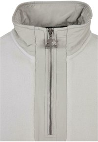 Fleece-pull i lys grå med høy krage, med kort glidelås og sølvfarget glidelåshåndtak med stjernelogodetalj.