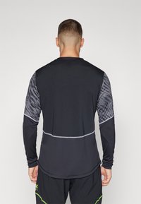 Langarm-Sportshirt in Schwarz mit grauem Muster an den Schultern und segmentiertem Design. Ausgestattet mit kontrastierenden Nähten und einem flexiblen Material.