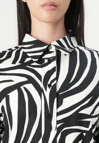 Camicia a righe bianche e nere con colletto a punta, dotata di chiusura frontale con bottoni e una texture di tessuto liscia.