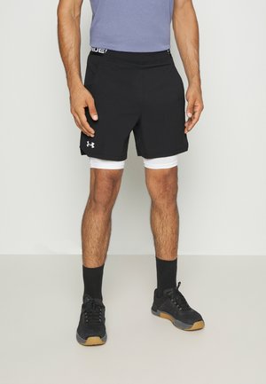 Schwarze Sportshorts mit einem elastischen Bund, kombiniert mit weißen Kompressionsshorts. Getragen mit schwarzen Socken und Sneakers, die ein strukturiertes Design aufweisen.