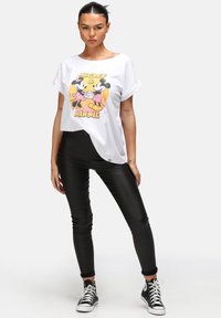 Camiseta blanca con un gráfico colorido de Mickey y Minnie Mouse, combinada con pantalones negros ajustados y zapatillas negras de caña alta.