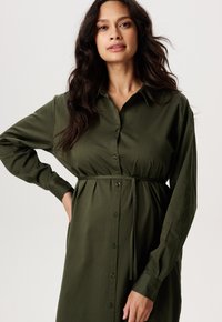Grünes Hemdblusenkleid aus leichtem Stoff, mit tailliertem Schnitt und Bindegürtel, langen Ärmeln und glatter Textur.