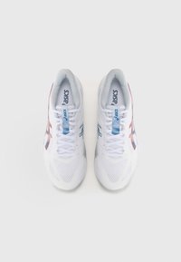 Baskets blanches de sport avec une tige en maille, présentant des accents bleus et rouges, des motifs circulaires sur la semelle et un design traditionnel de lacets.